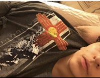 a young man laying in bed with a flag on his shirt